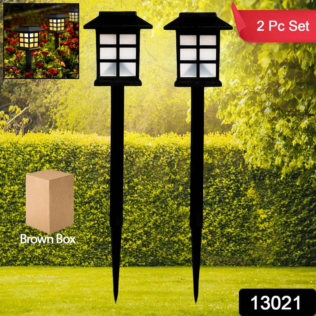 Two black solar garden lights with white paneled tops stand in a vibrant green lawn with hedges and trees.