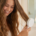 Hand pressing the quick-release button on the Self-Cleaning Hair Brush to remove trapped hair.